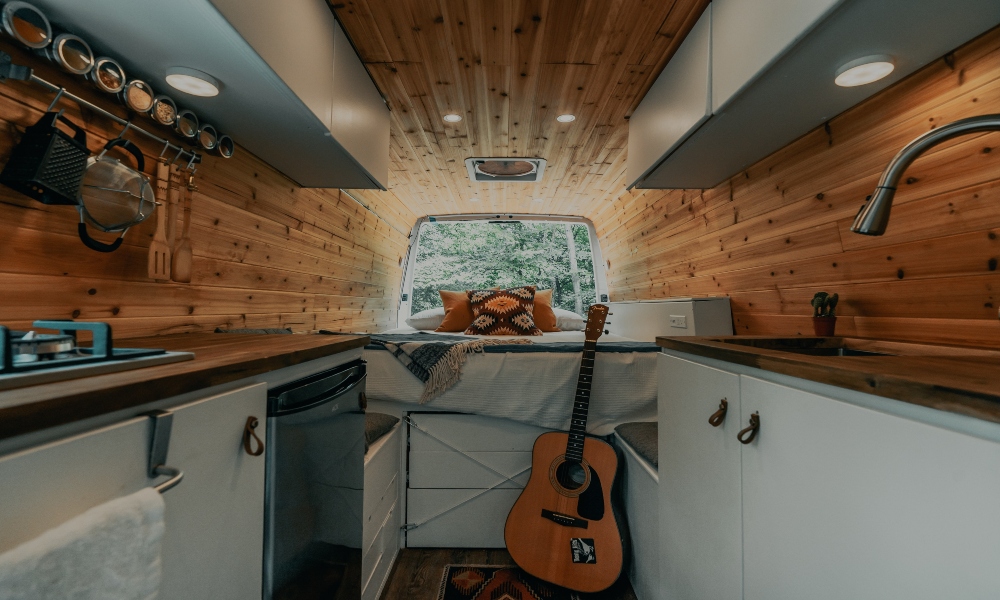 Inside of a renovated van, wood panelling, guitar leaning against bed