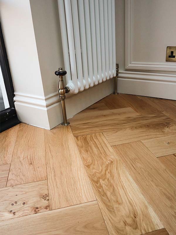 white skirting board, herringbone floor and white radiator with brass pipes