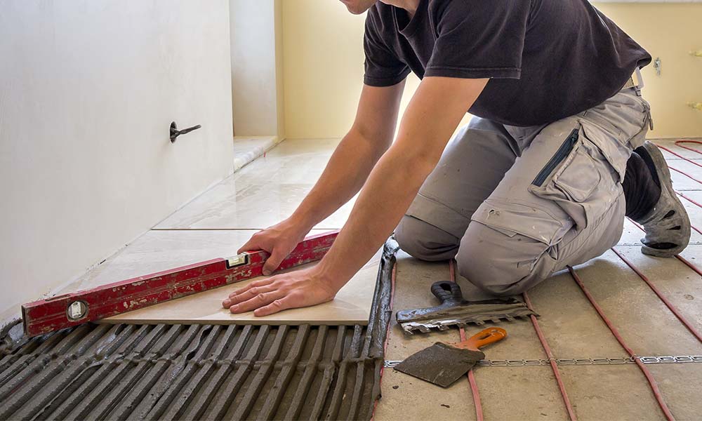 man installing tiles over conv=crete and underfloor heating 