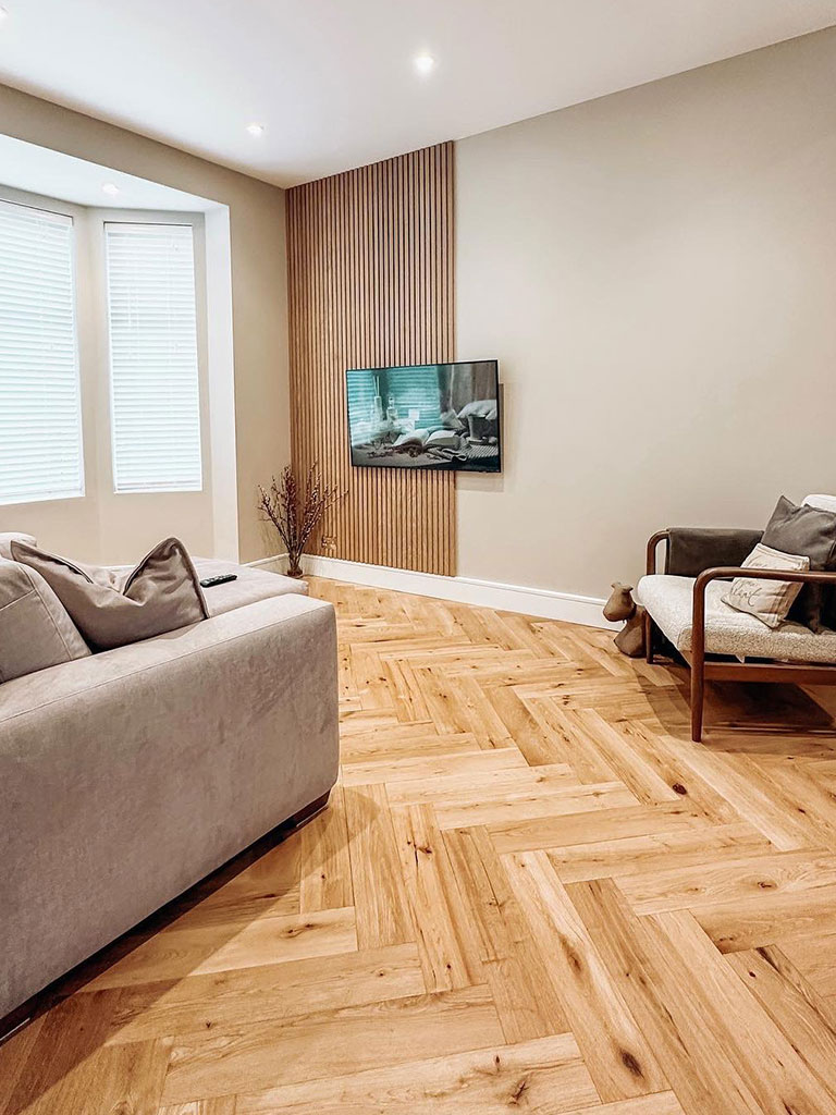 Living room with golden herringbone flooring with tv on wall and grey sofa with modern arm chair