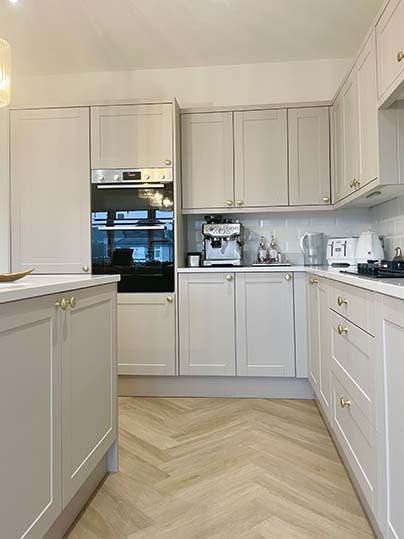Close up of pale coloured kitchen with gold detailing and herringbone floor