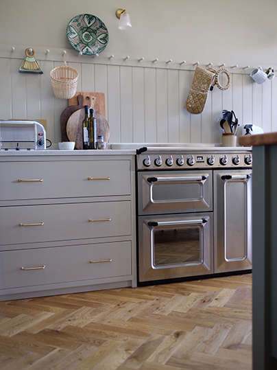 Kitchen with pale tones cabinets, silver cooker and warm toned herringbone flooring
