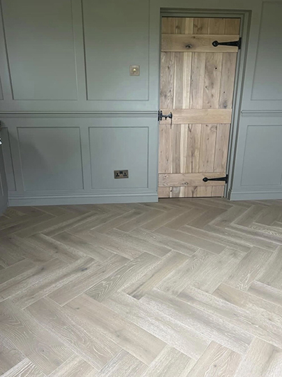 Close up detail of wooden door, sage green panelling and herringbone floor