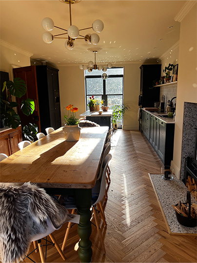 Cosy open plan dining room with warm toned herringbone floor and 10 seater wooden table